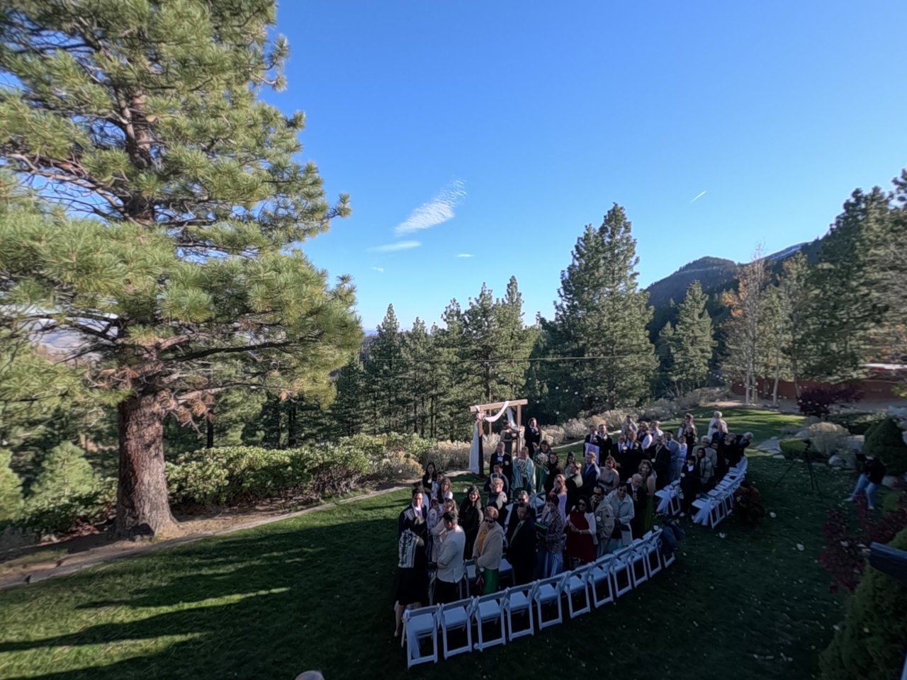 Guests on their feet on the lawn at the close of the ceremony, the pines and mountains around them