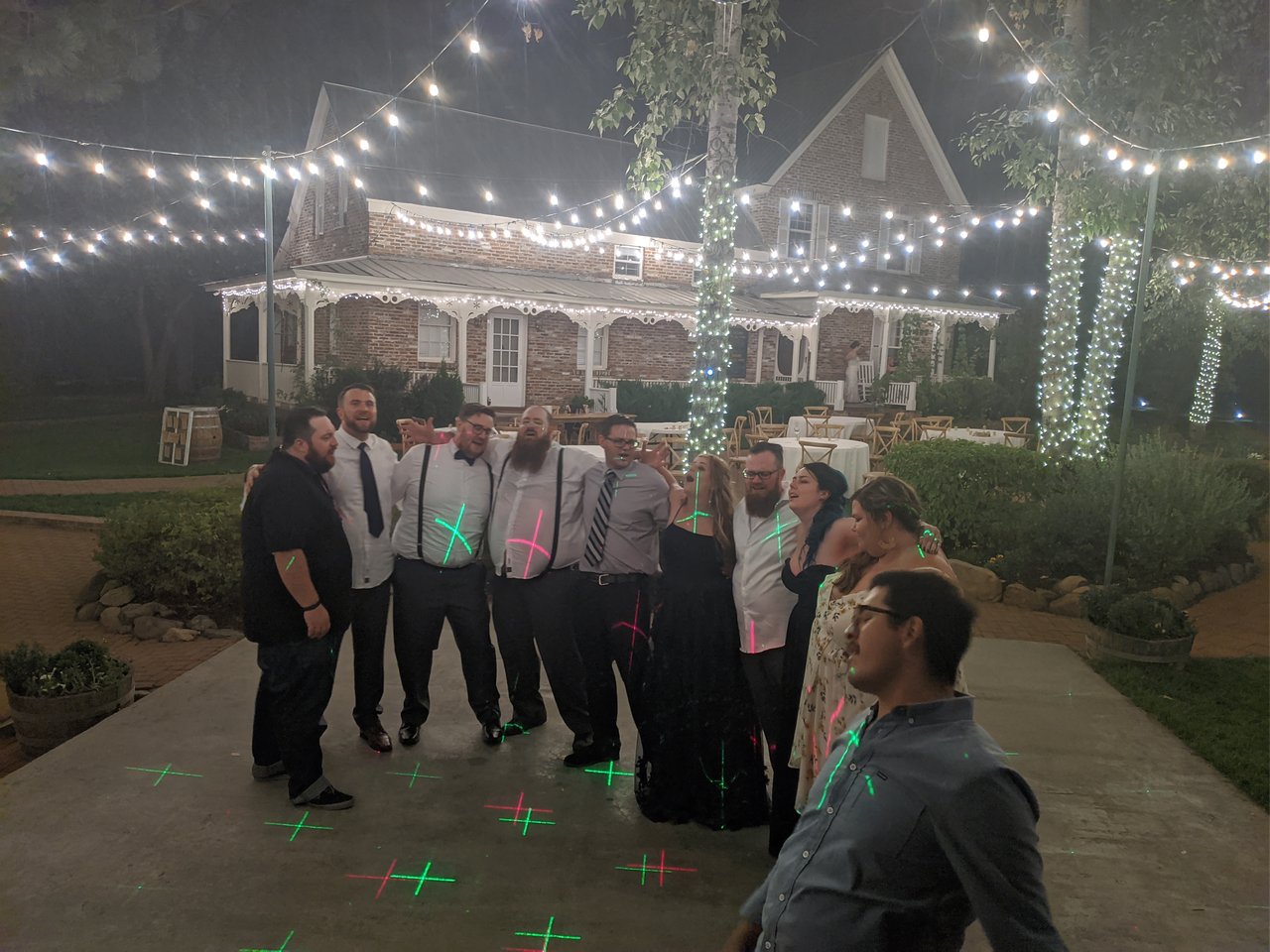 Guests arm in arm singing Bohemian Rhapsody under string lights and laser lights in front of the brick house