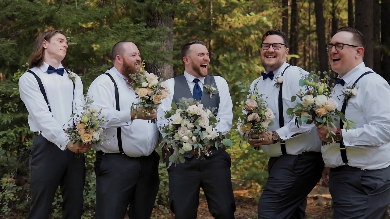 The groomsmen laugh while holding bouquets in the pines