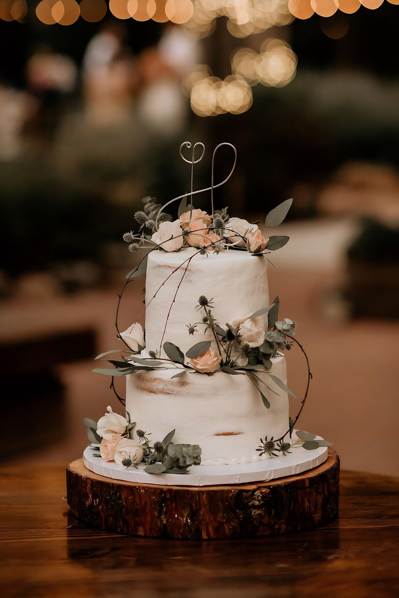 Their white wedding cake with flowers and a wire topper on a wood slice, photo by Woodmancy Photography