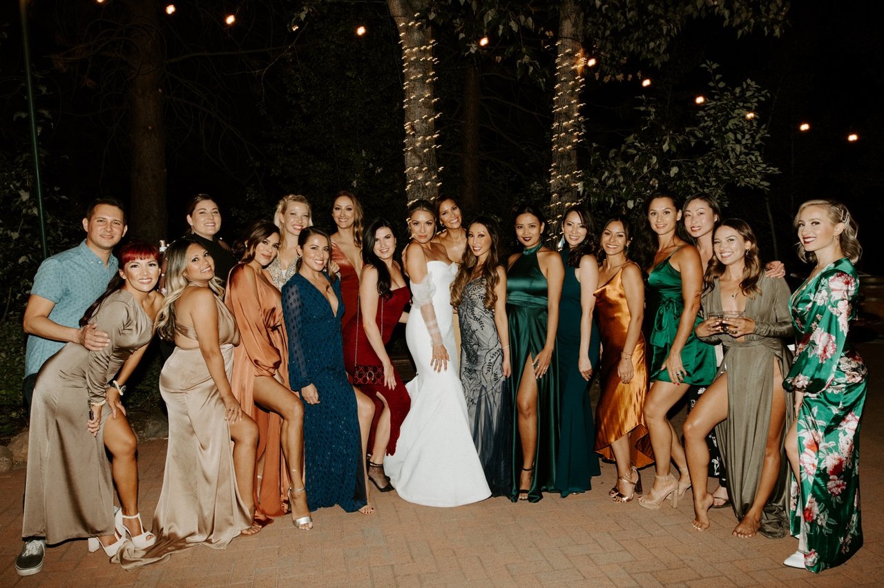 Joan with a big group of friends in velvet and satin dresses under the string lights