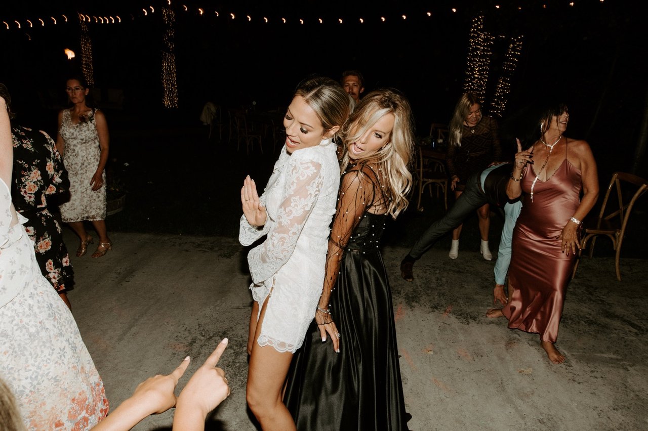 Joan in her lace reception dress dances with a friend on the dance floor
