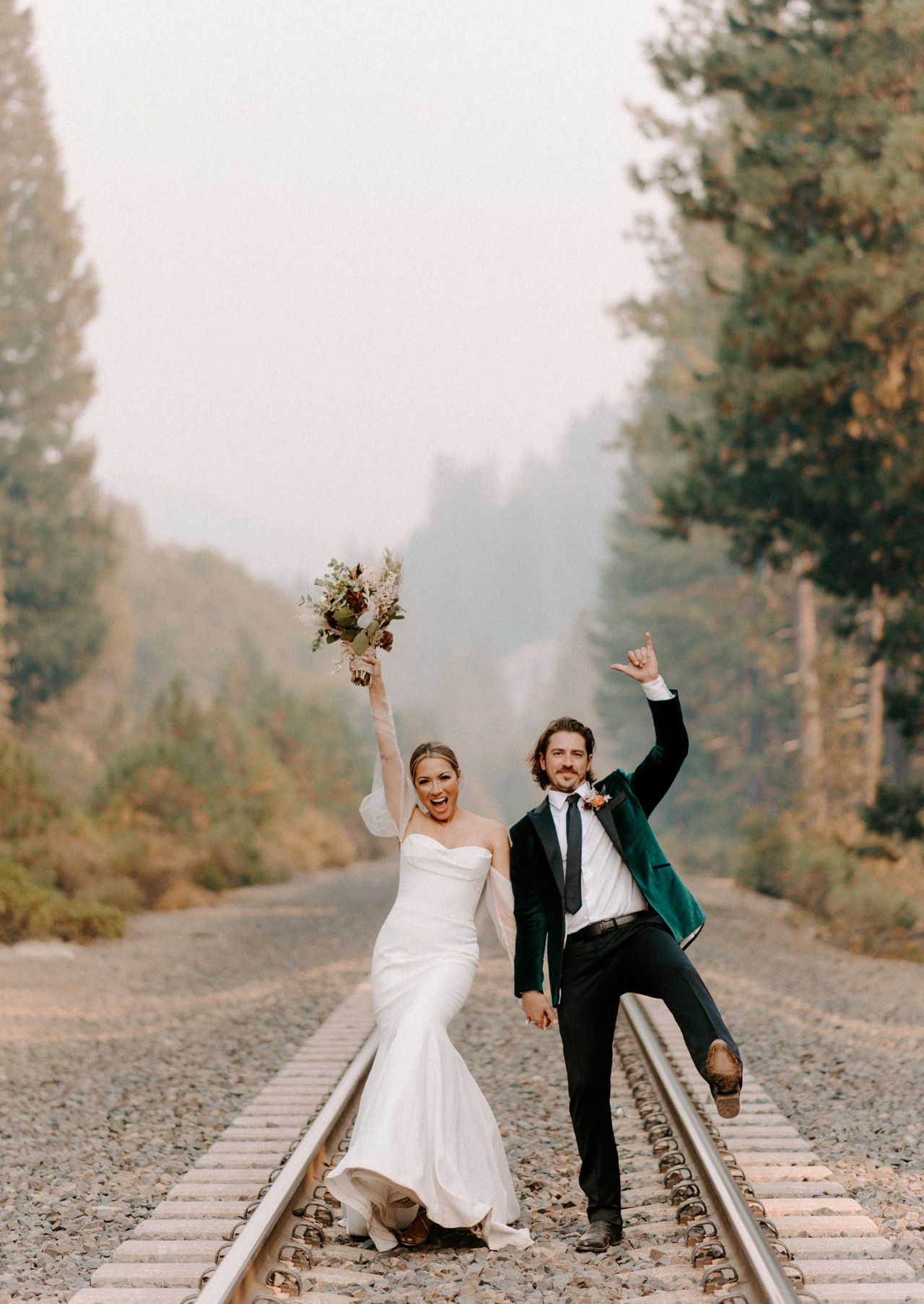 Joan and Kyle jump and cheer on the railroad tracks