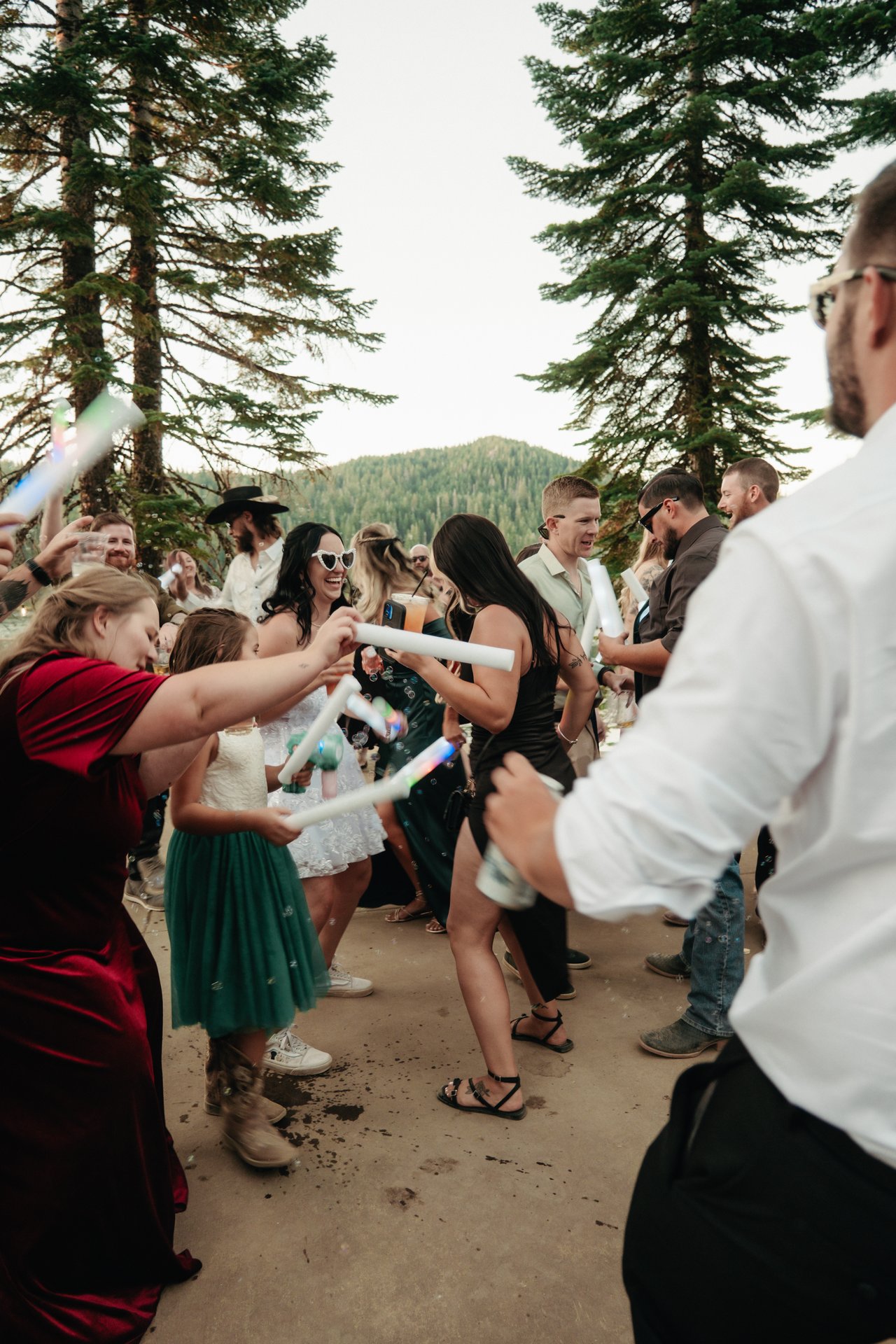 Kaitlyn laughs in heart sunglasses as friends swing foam batons through drifting bubbles under the pines