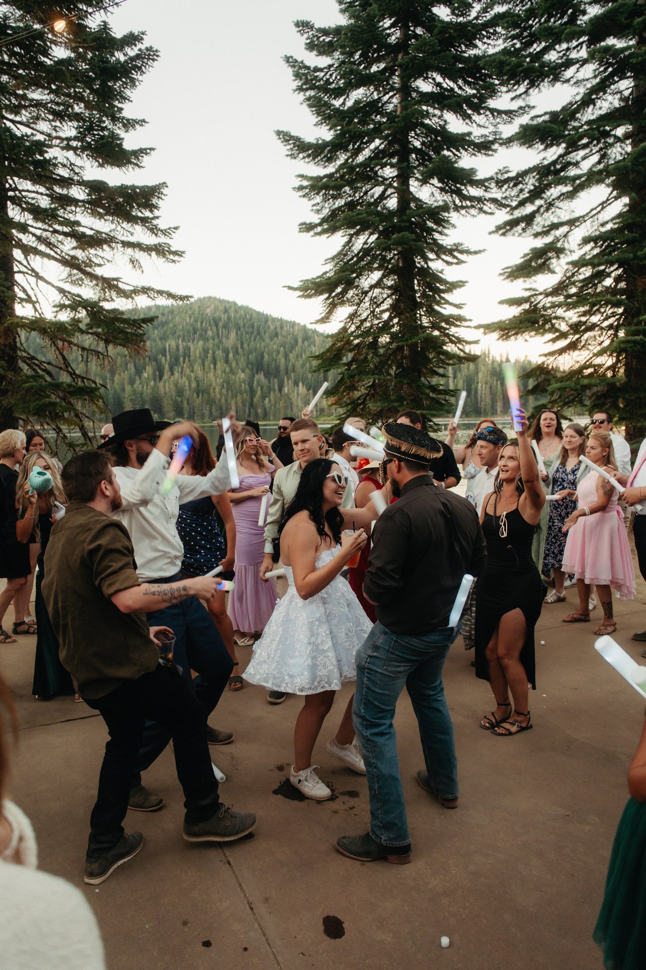 Kaitlyn dances with a man in a fringed hat, tall pines and a forested mountain behind them