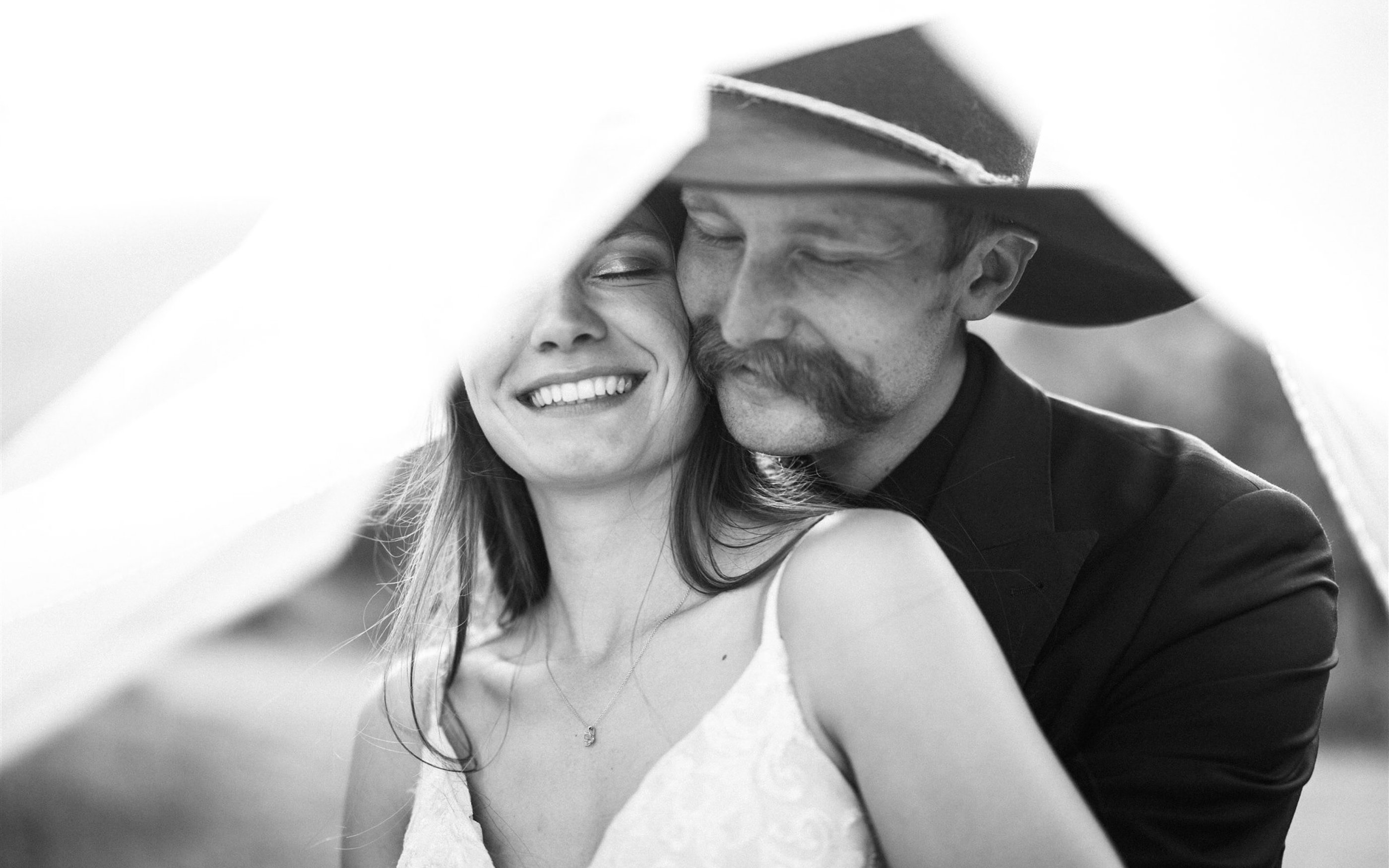 Kerstyn and Jakob hold each other close under her veil, his cowboy hat tipped against her, in black and white