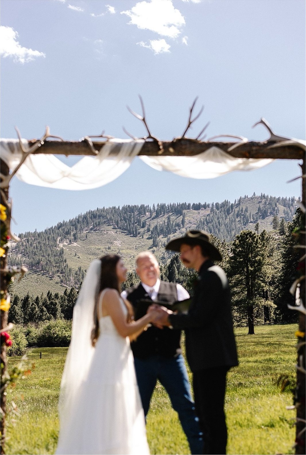 Kerstyn and Jakob hold hands with the officiant under the antler arch