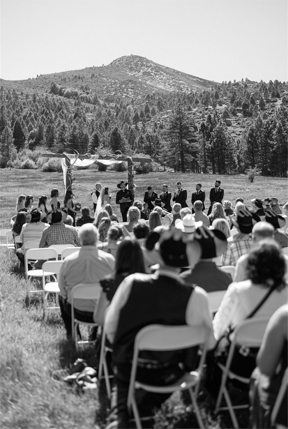 Guests watch the ceremony in the meadow at Nevada Star Ranch with the mountains behind, in black and white