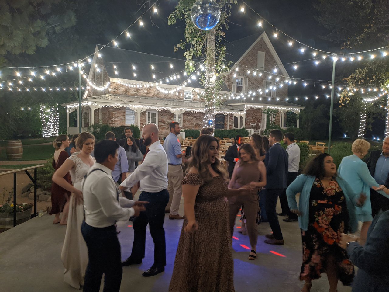 A full dance floor under the string lights in front of the brick house