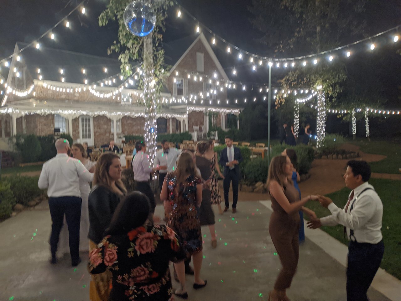 Guests start dancing under the string lights and disco ball in front of the brick house