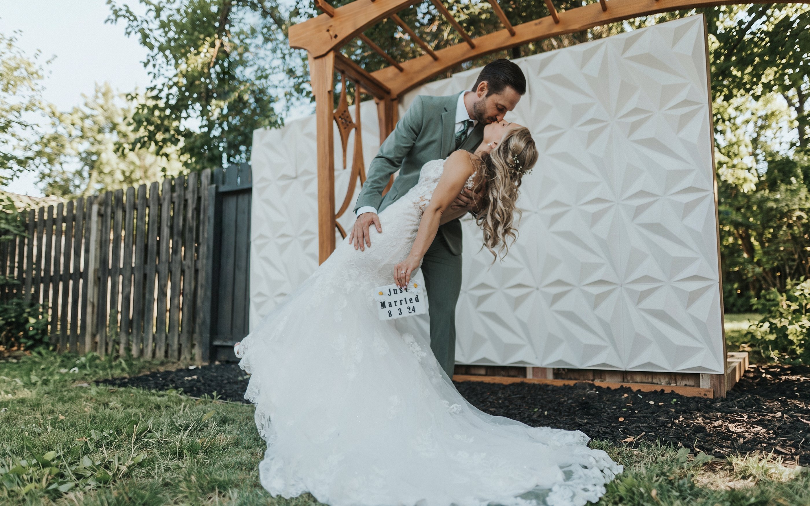 Jeremy dips Lexy for a kiss under the wooden arbor in their backyard