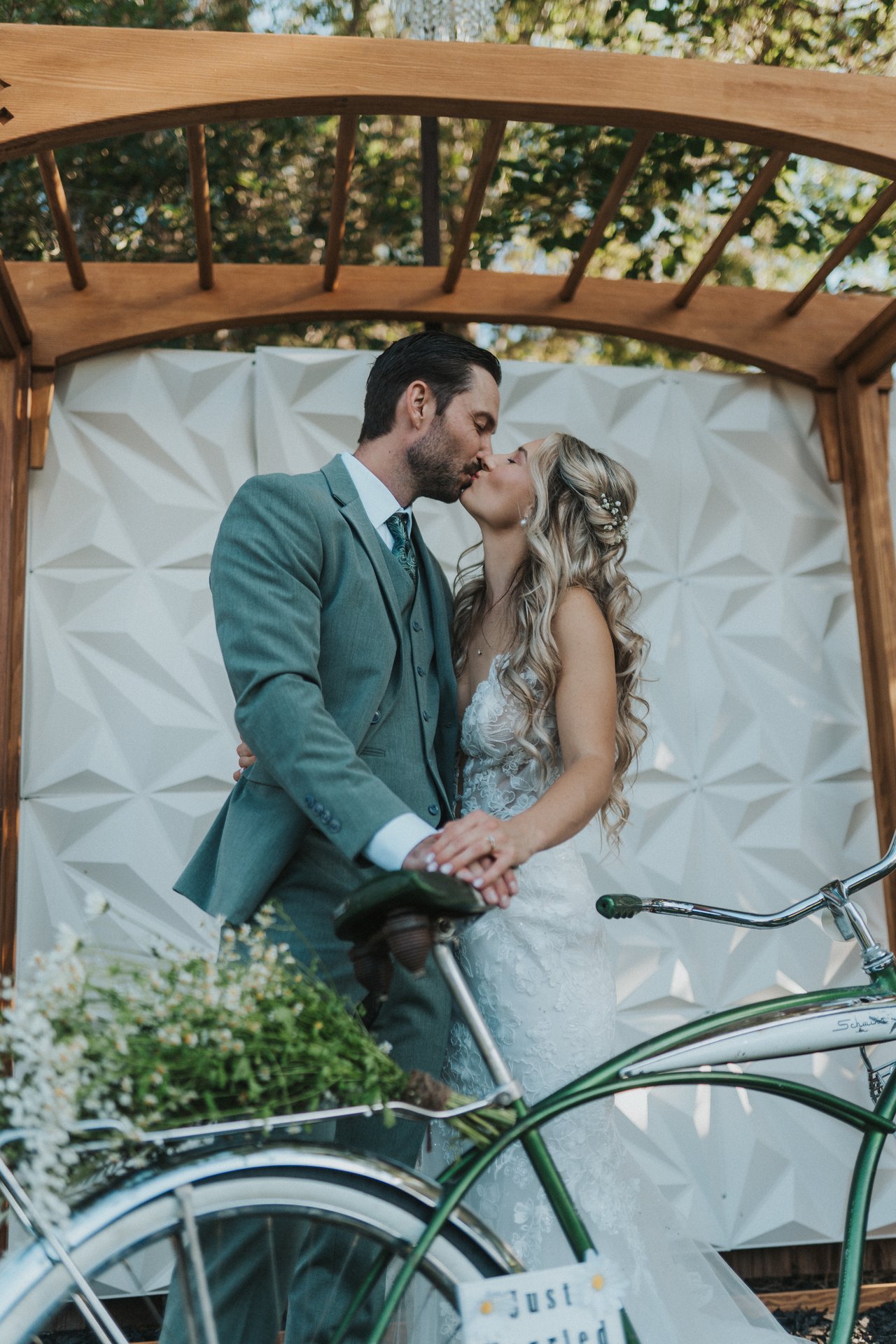 Lexy and Jeremy kiss over the bike under the arbor
