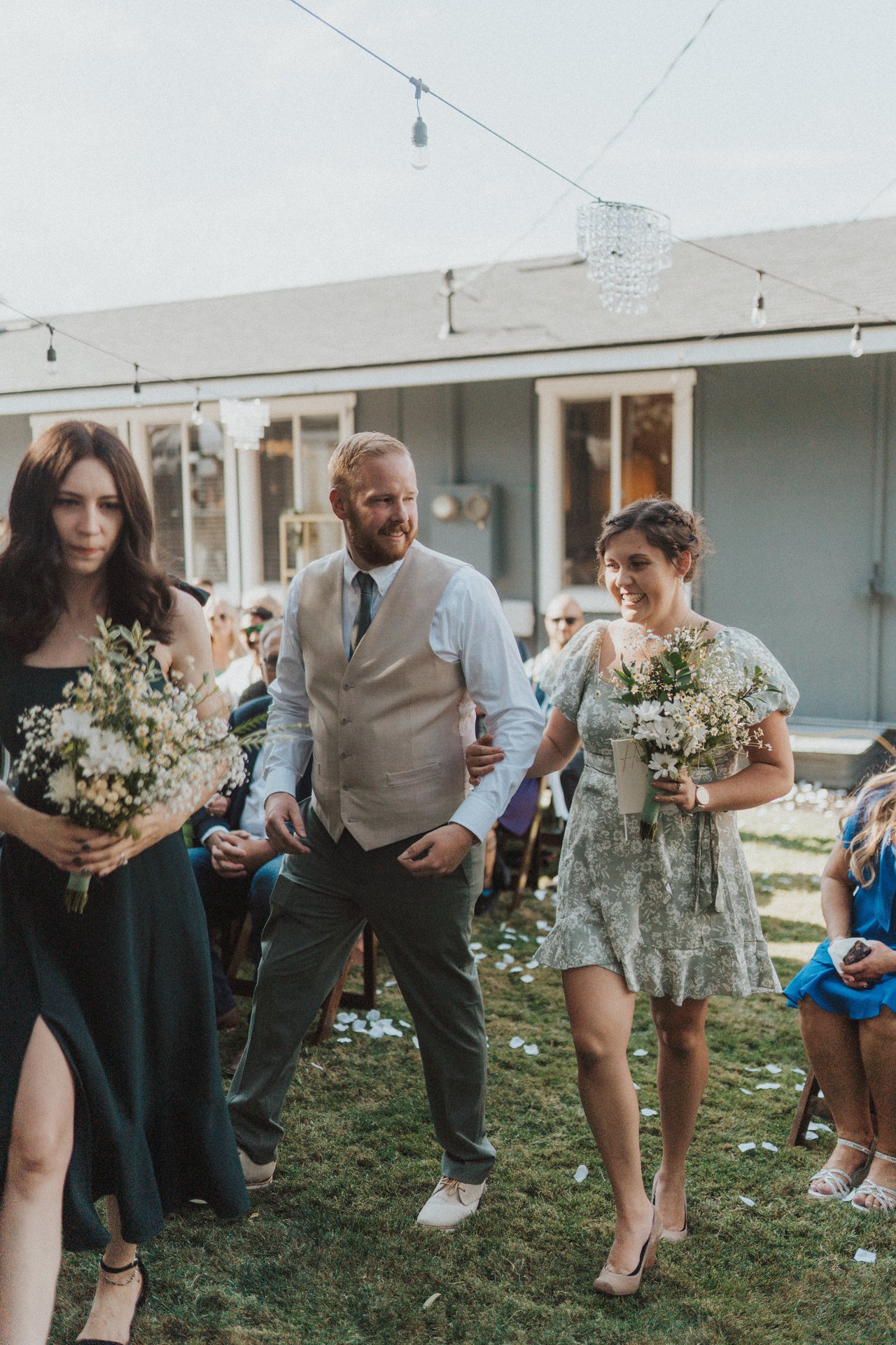 Two bridesmaids and a groomsman walk in with their bouquets