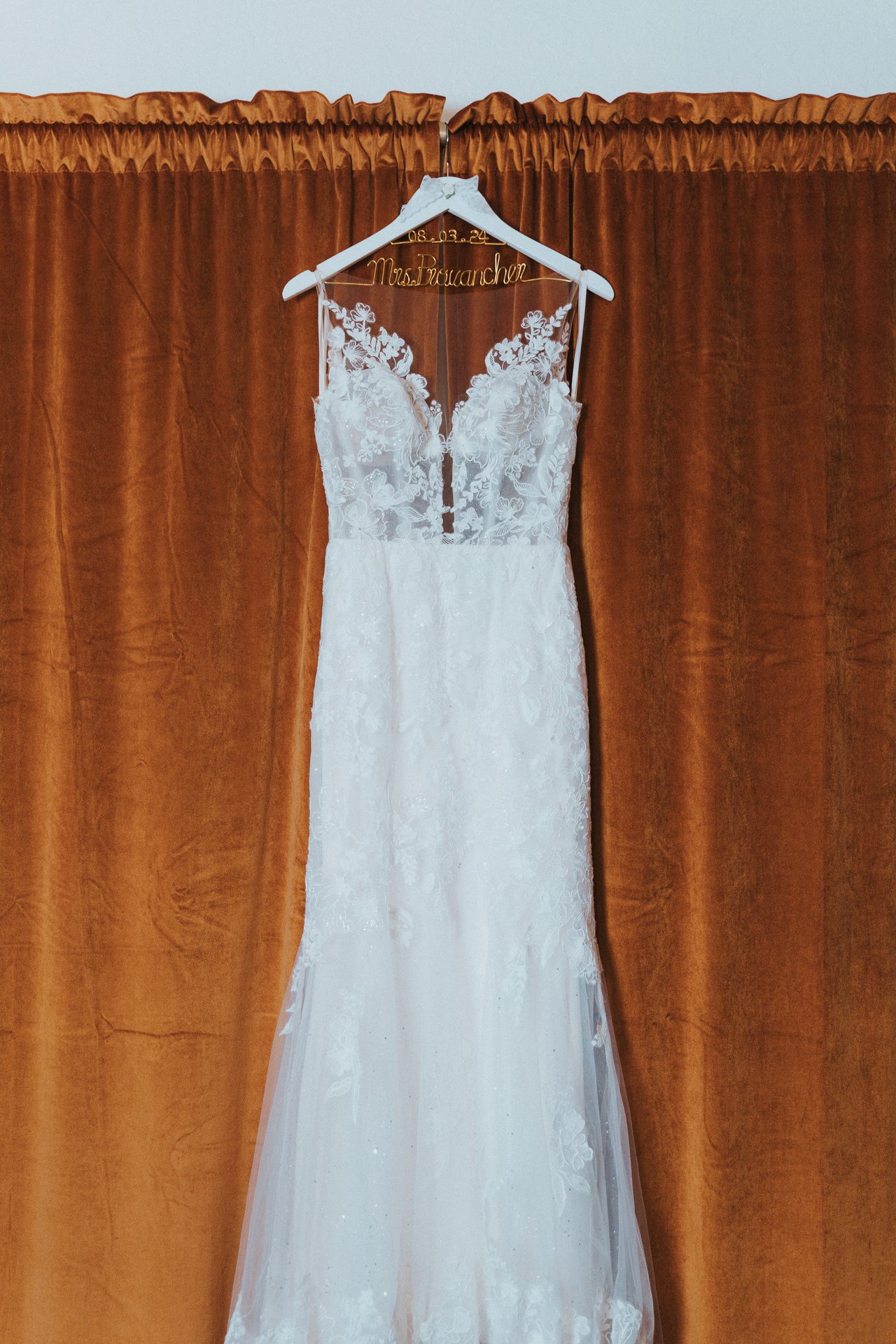 Lexy's lace wedding dress hanging against the rust curtain