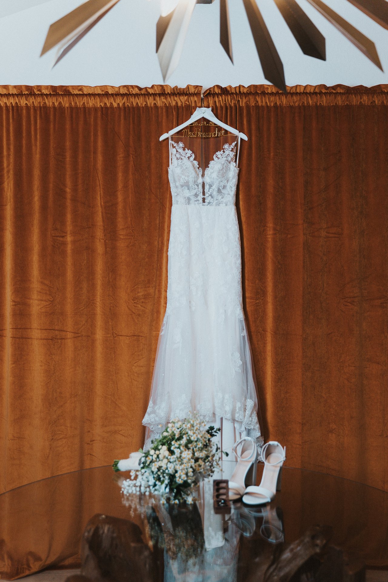 Lexy's wedding dress hanging against a rust velvet curtain