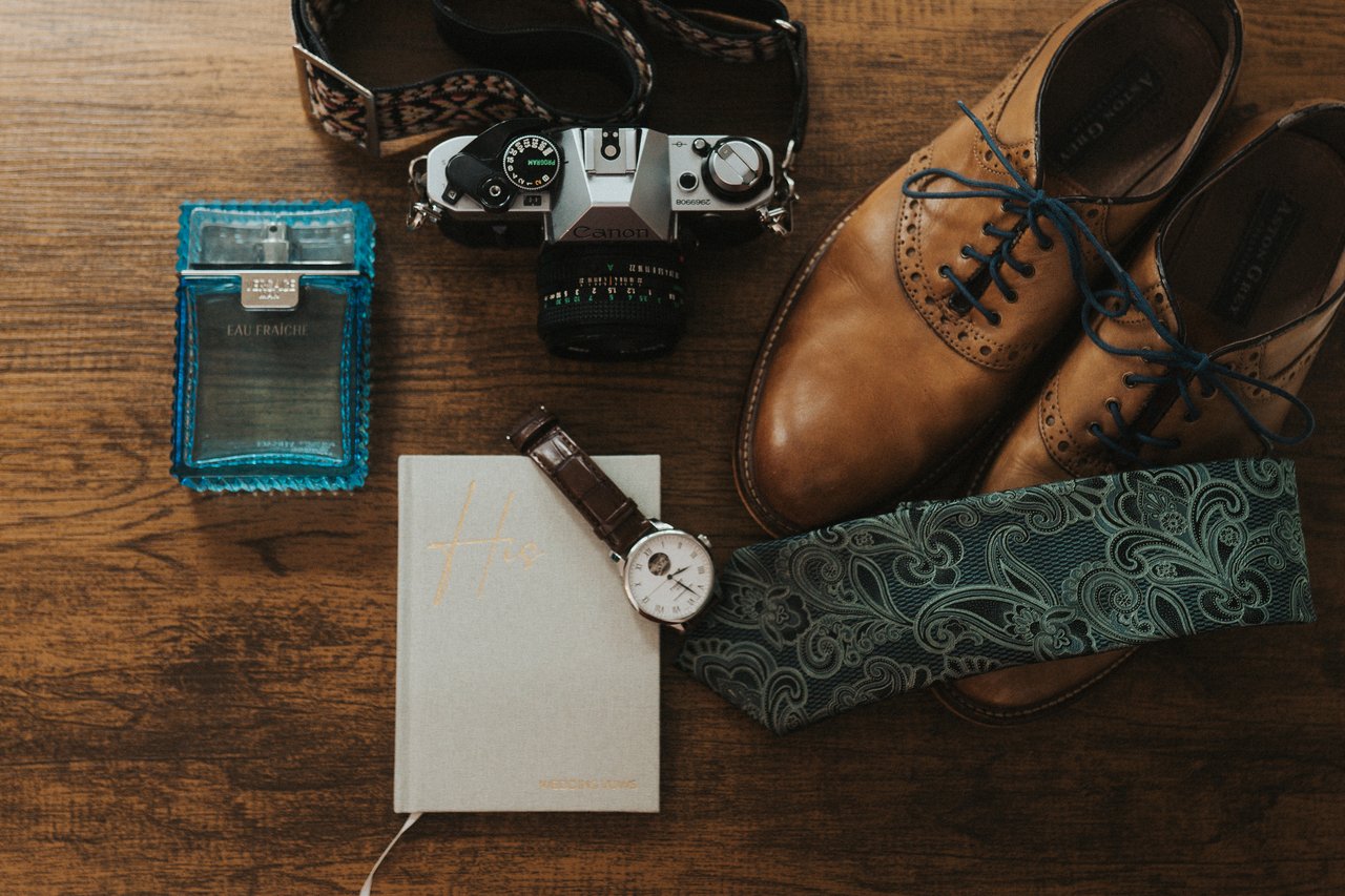 Jeremy's shoes, tie, watch, camera and cologne on a wood table