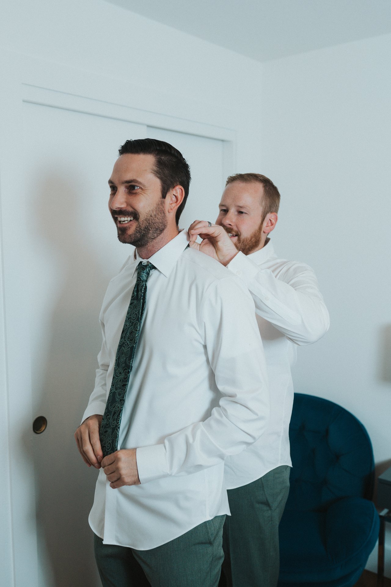 Jeremy laughing as a groomsman helps with his collar