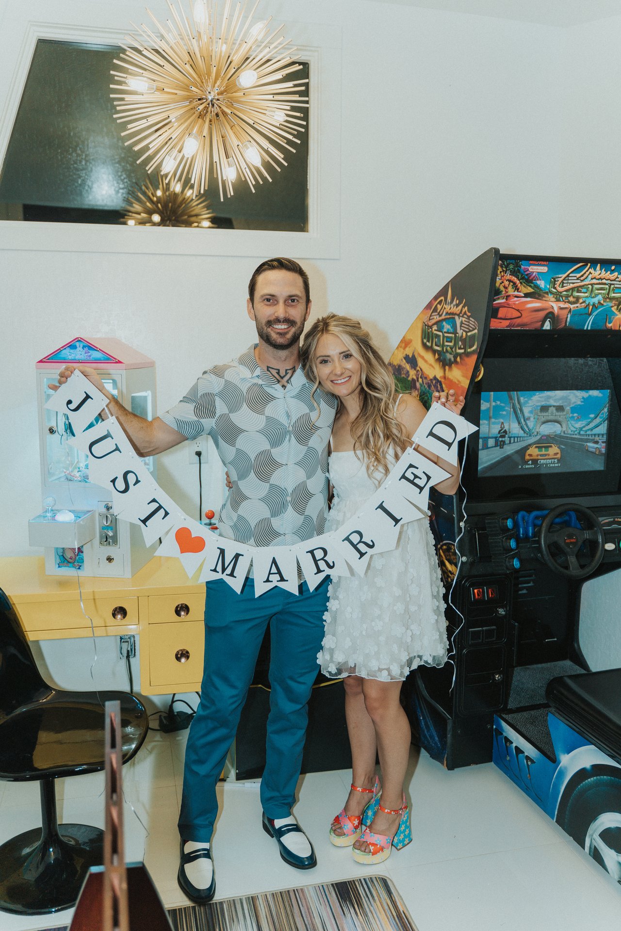 Lexy and Jeremy hold a Just Married banner in the arcade room