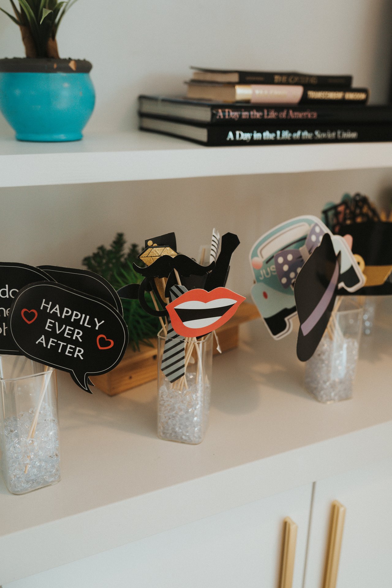 Photo booth props in glass cups on a white shelf