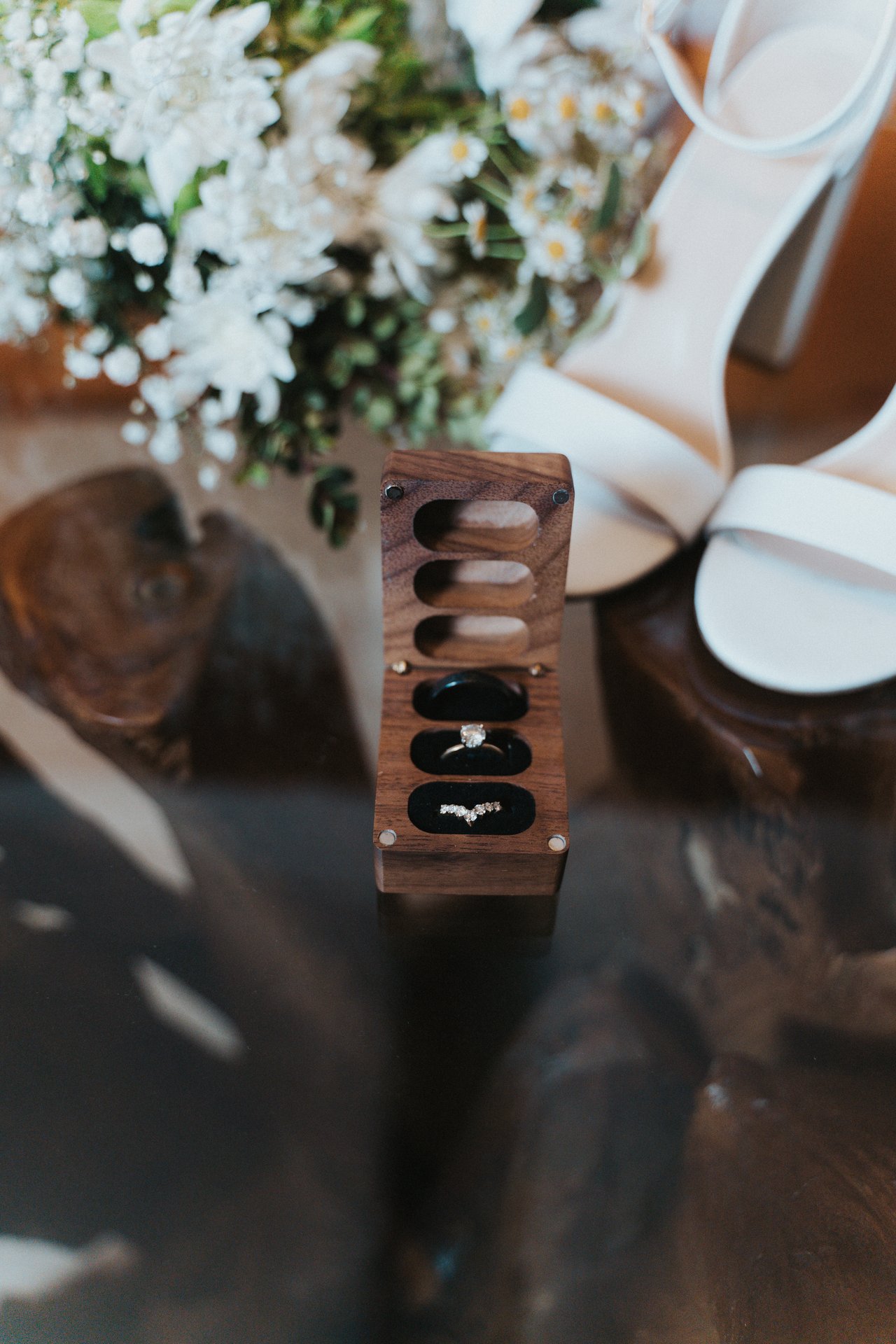 The wedding rings in a wooden box beside the bridal heels