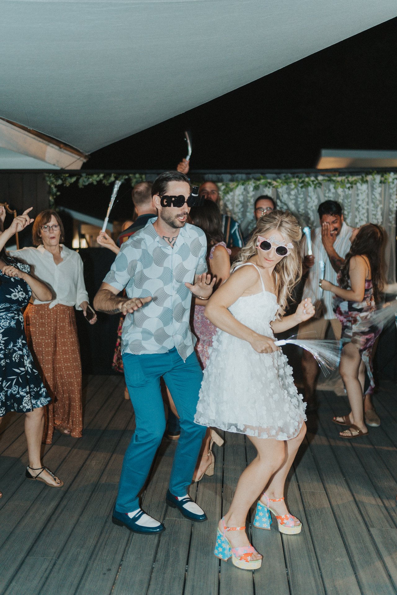 Lexy and Jeremy dancing in novelty sunglasses under the shade sail