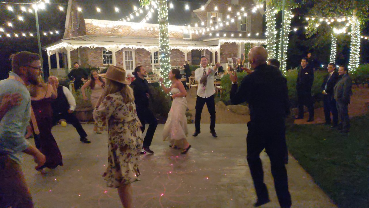 The bride dancing with guests under the string lights in front of the brick house at Twenty Mile House