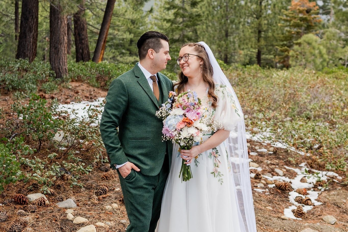 Madison and Adam stand together in the pines with patches of snow behind them, photo by GOT Photography