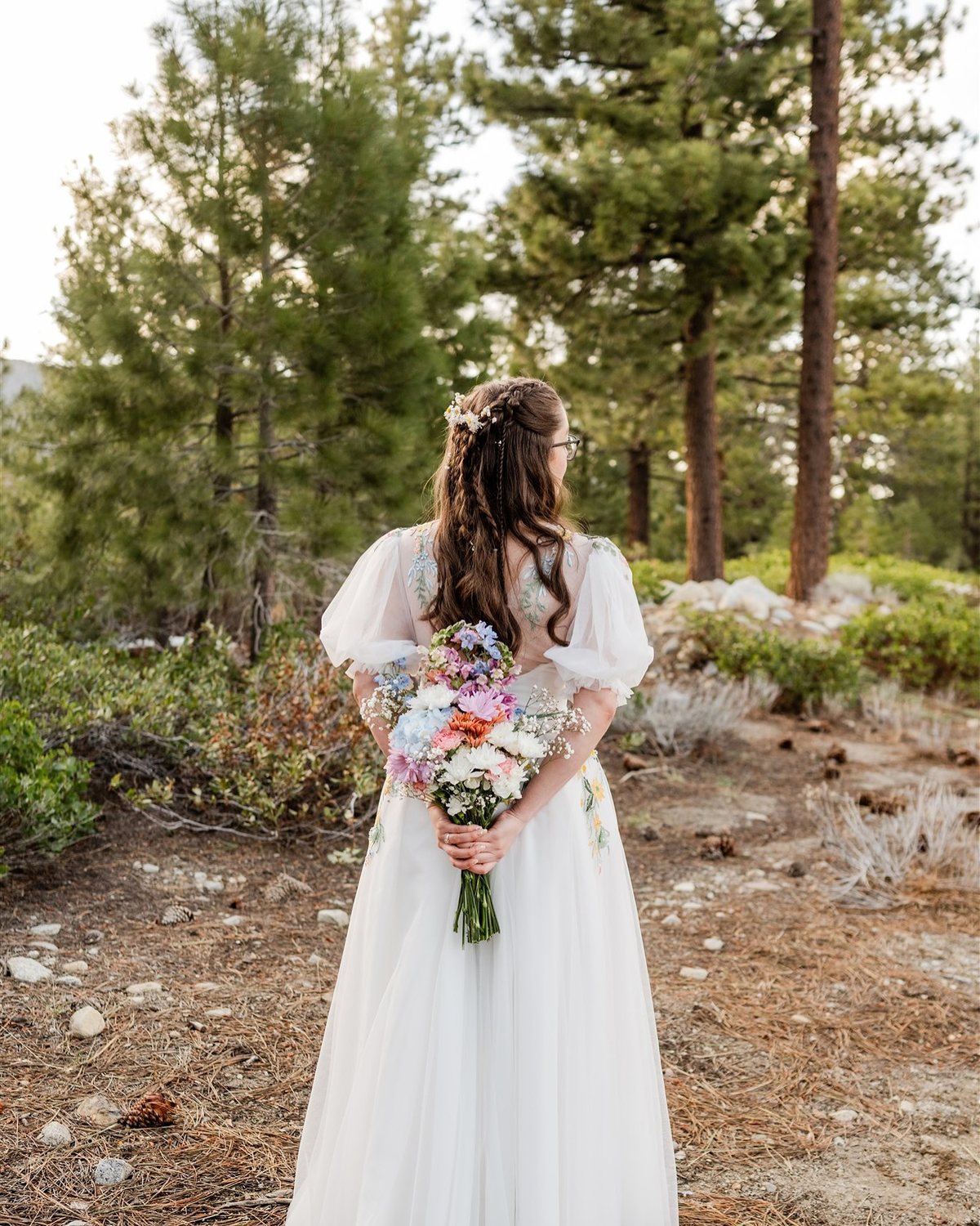 Madison holds her wildflower bouquet behind her back among the pines