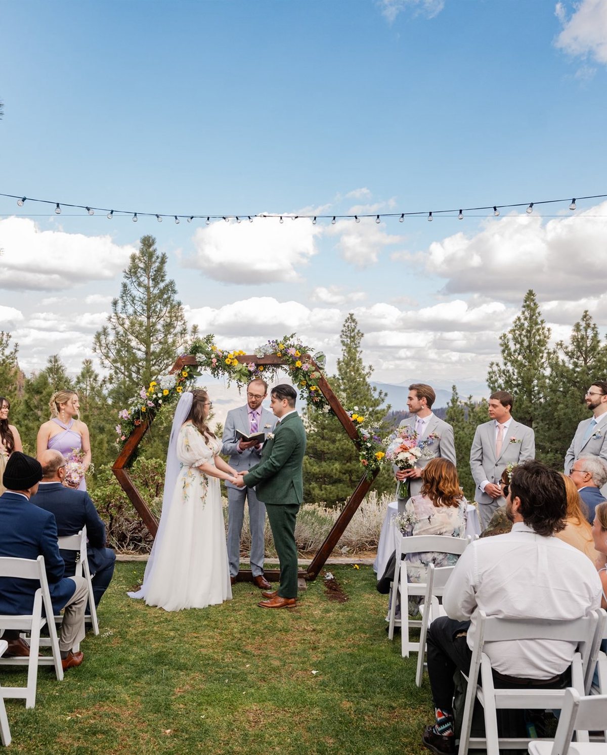 Madison and Adam hold hands at the hexagon arch under string lights during their ceremony