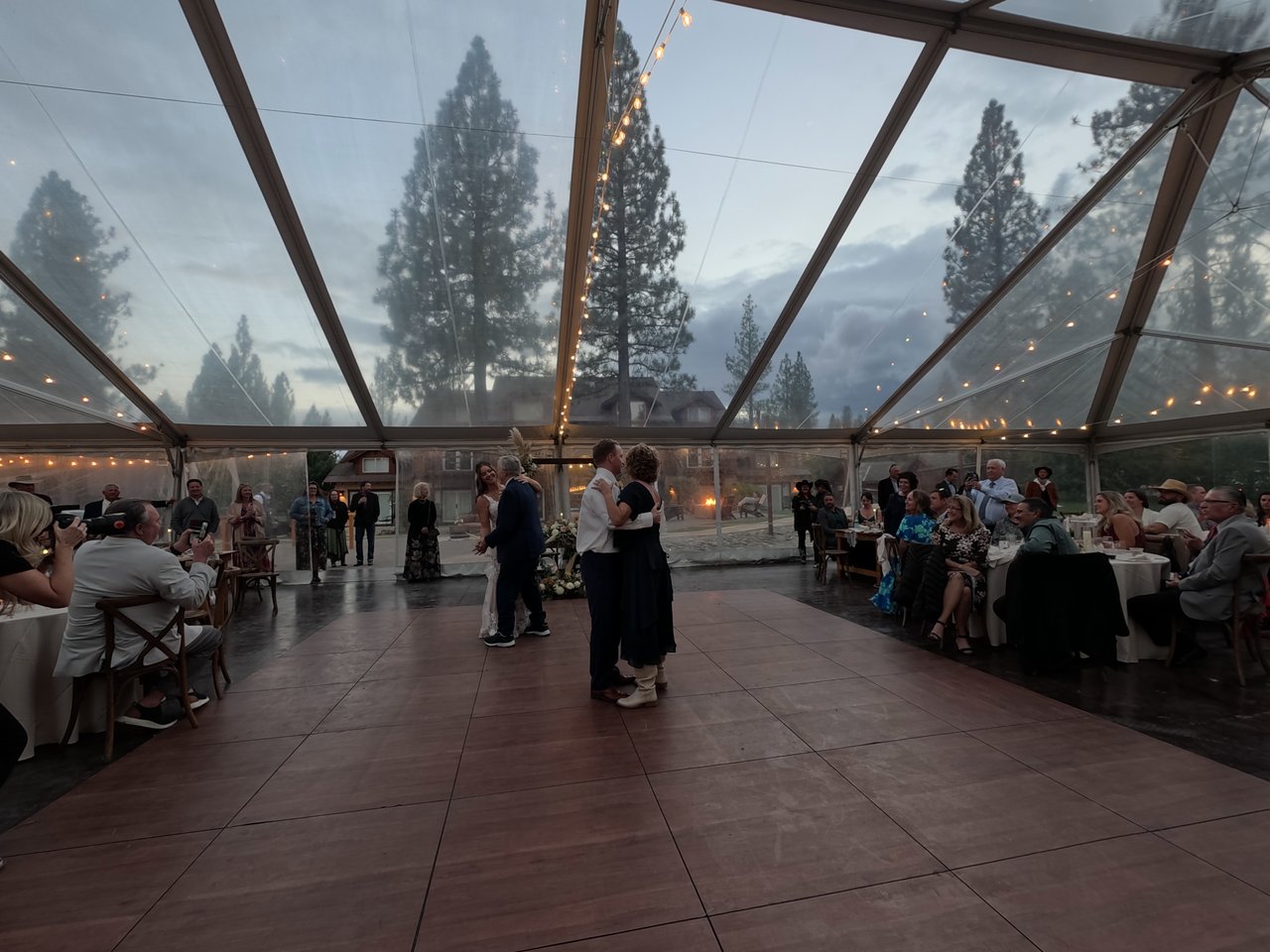 Matt dances with his mother under the clear tent at dusk as guests look on