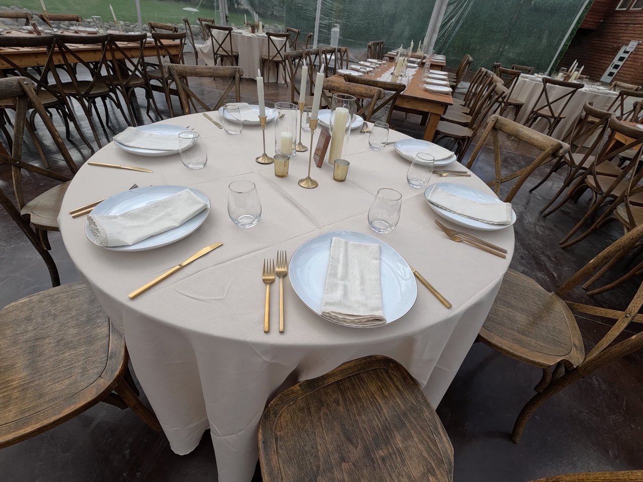 A round table set with gold cutlery, white napkins and candles under the clear tent at Chalet View Lodge