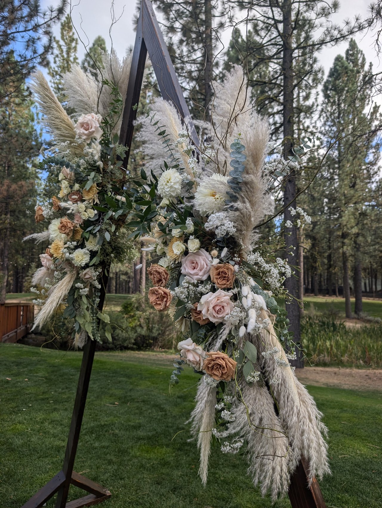 Pampas grass, roses and greenery on the wooden ceremony arch in the pines