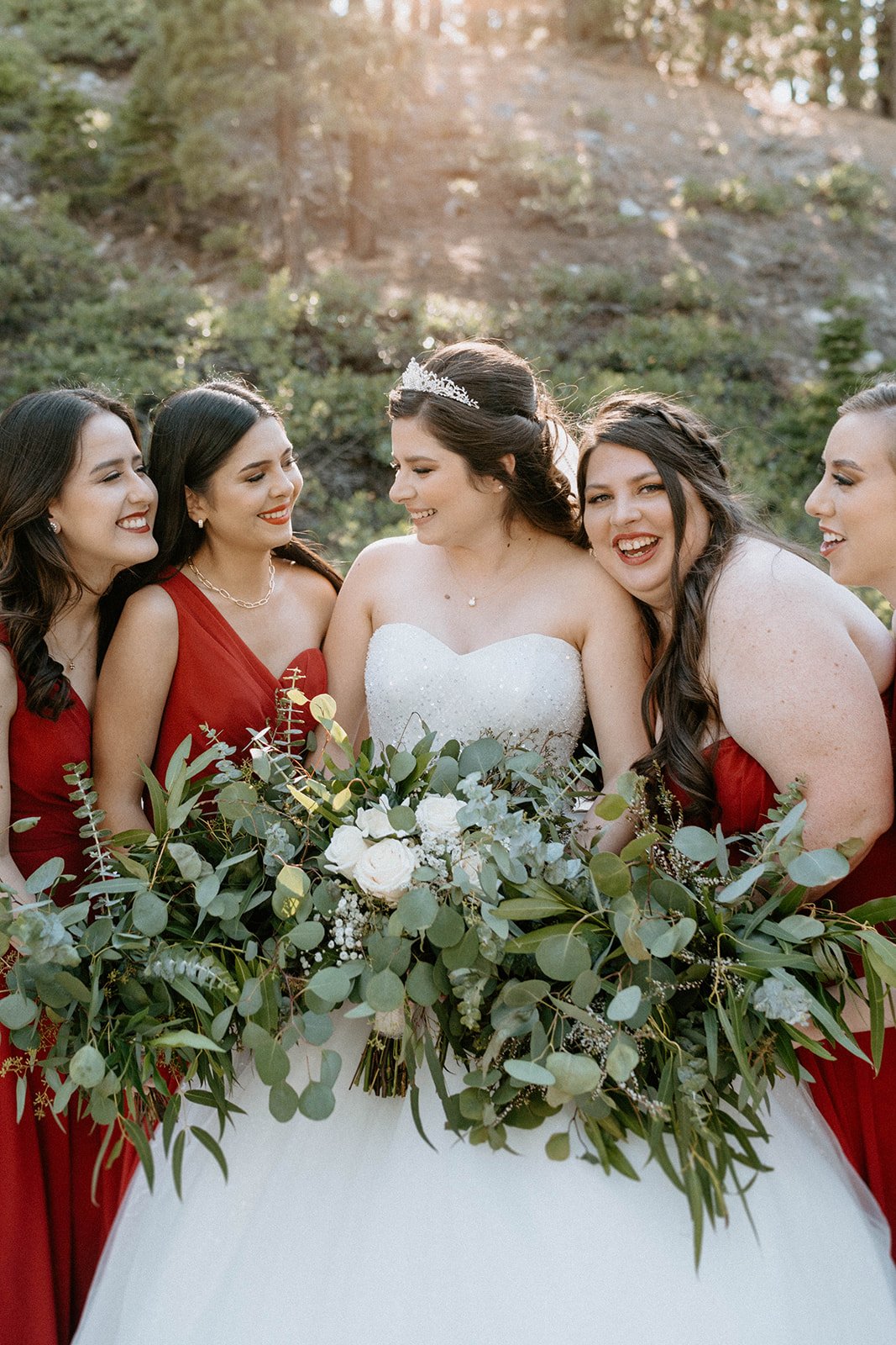 Montse laughs with her bridesmaids, a big bouquet of greenery in front of her
