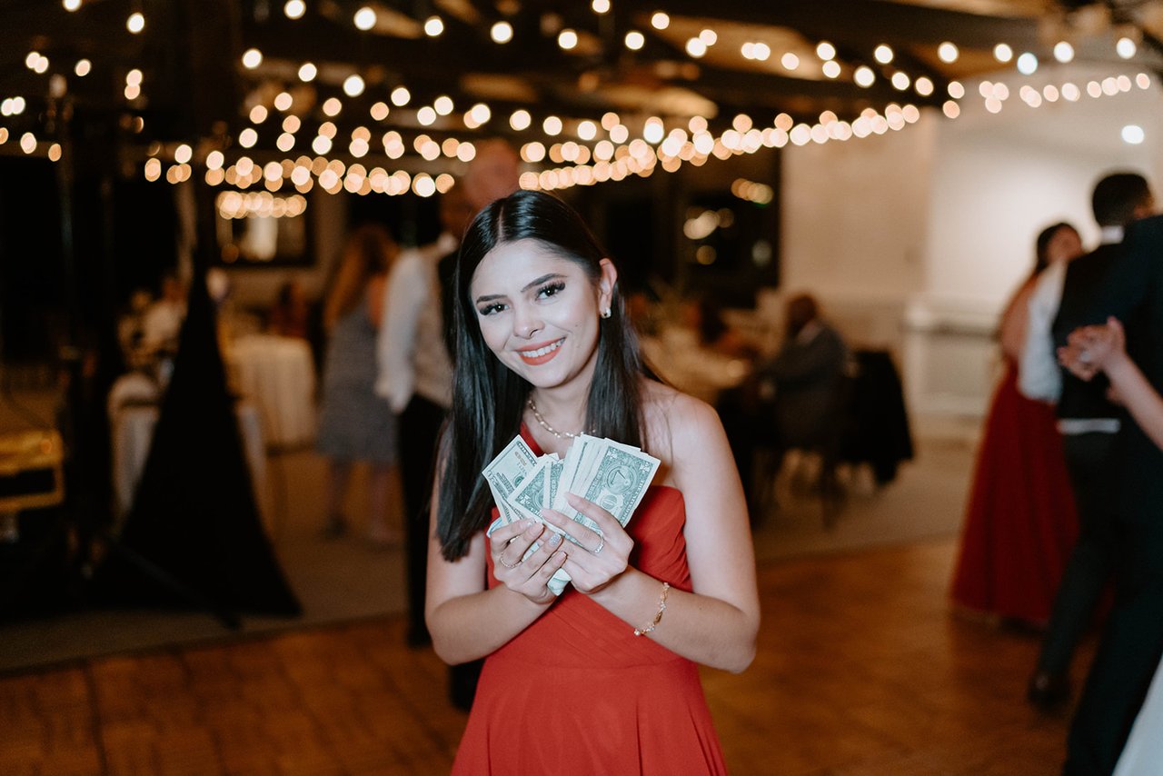 A bridesmaid in red shows off a fan of dollar bills