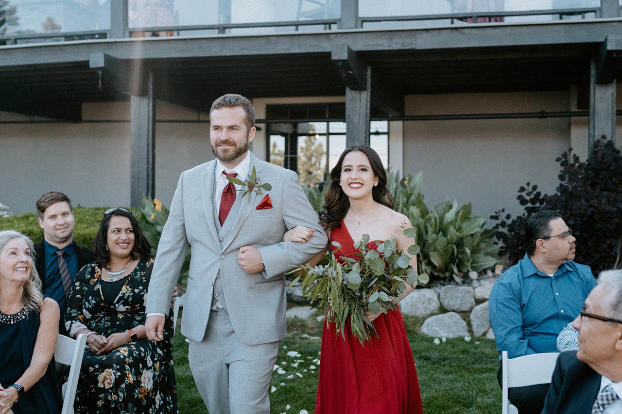 A bridesmaid in red and a groomsman walk down the aisle