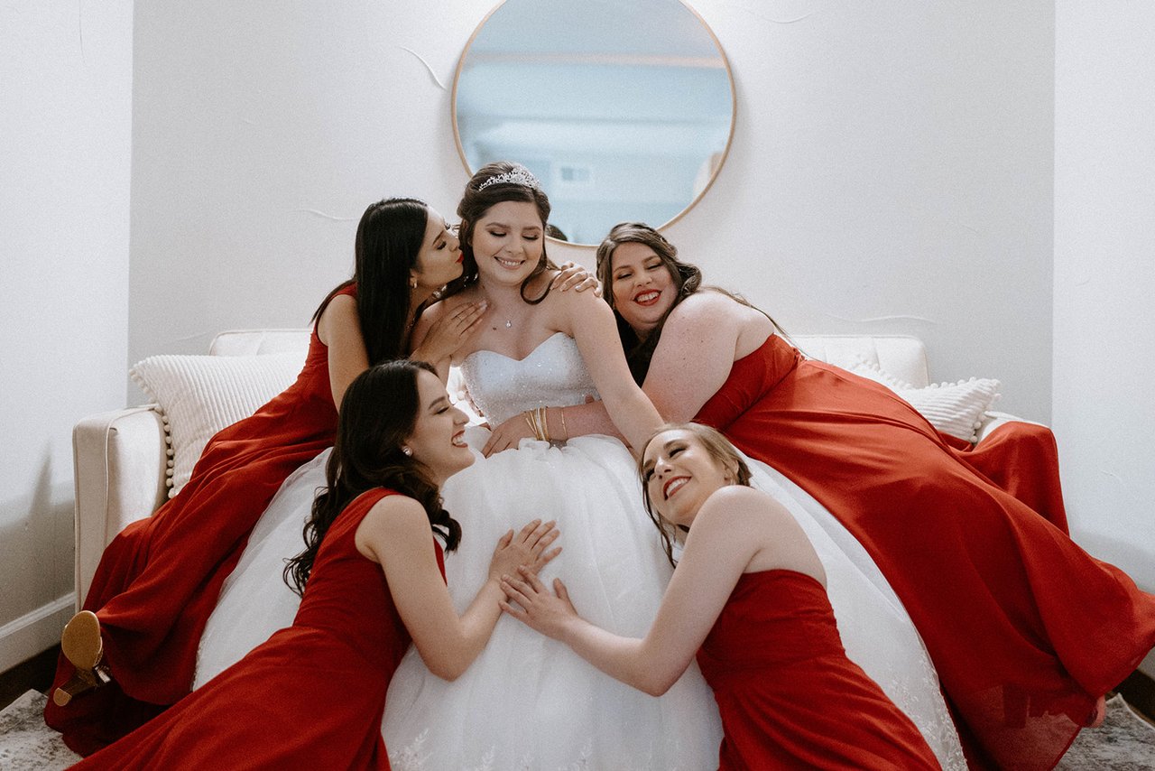The bridesmaids in red lie around Montse's ball gown, laughing