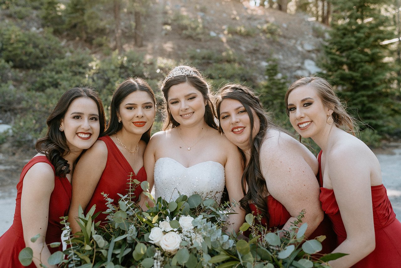 Montse and her bridesmaids in red lean in close with their eucalyptus bouquets