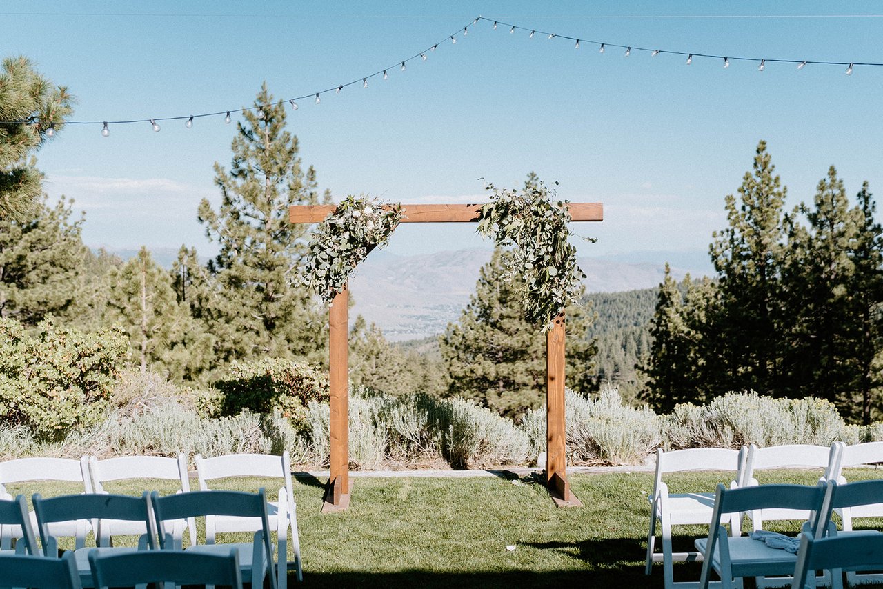The wooden arch and white chairs on the lawn with the valley and pines behind