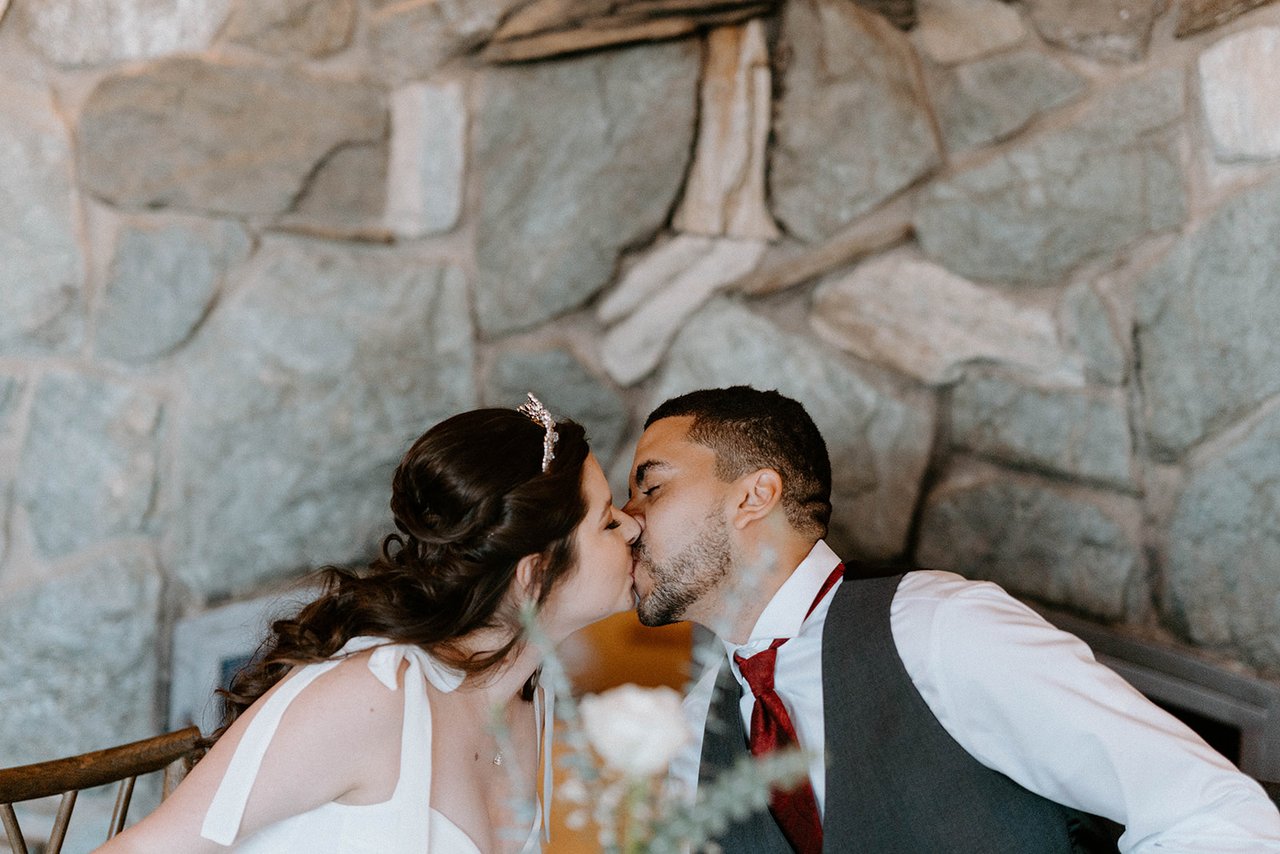 Montse and Jason kiss in front of the stone fireplace