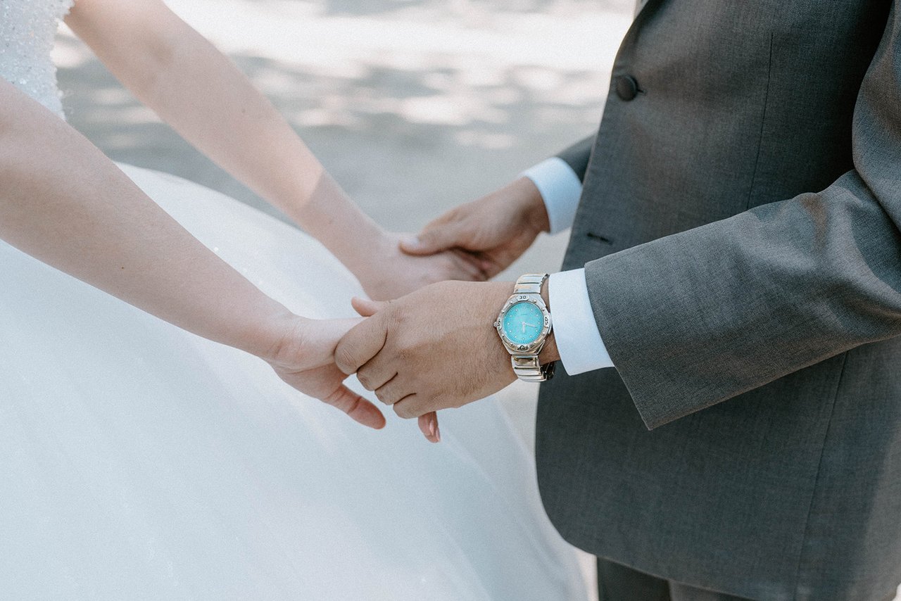 Montse and Jason hold hands, his watch and her lace close up