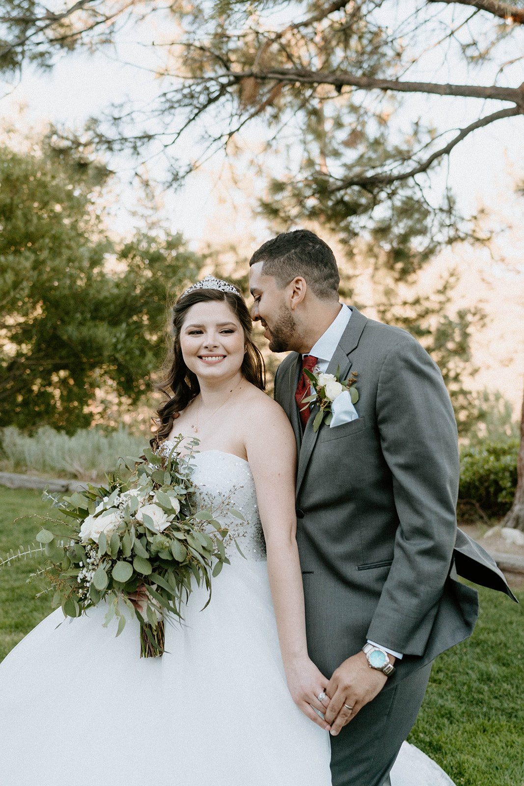 Montse smiles as Jason kisses her temple, her bouquet of greenery in hand