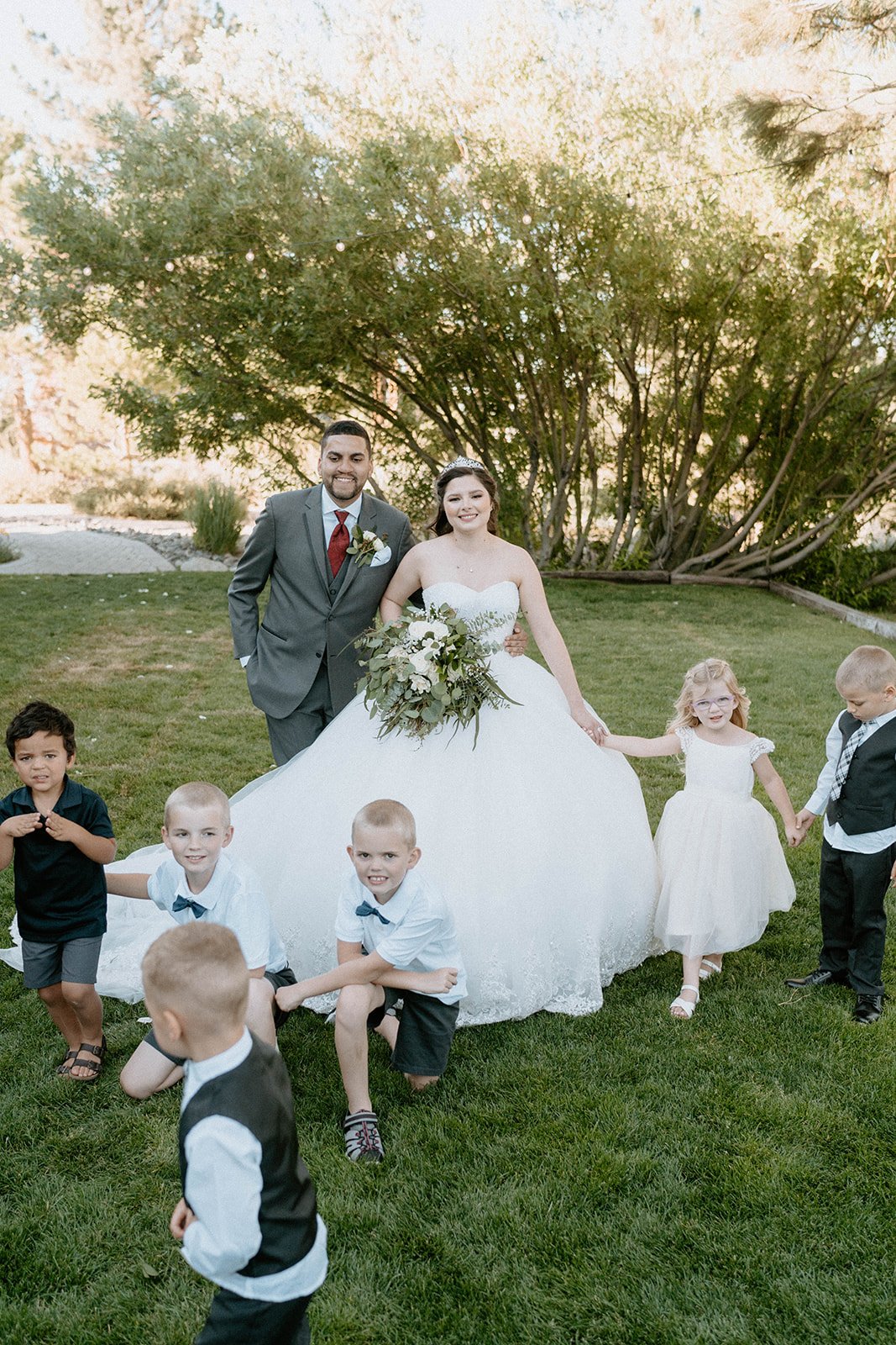 The flower girls and ring bearers run around Montse on the lawn