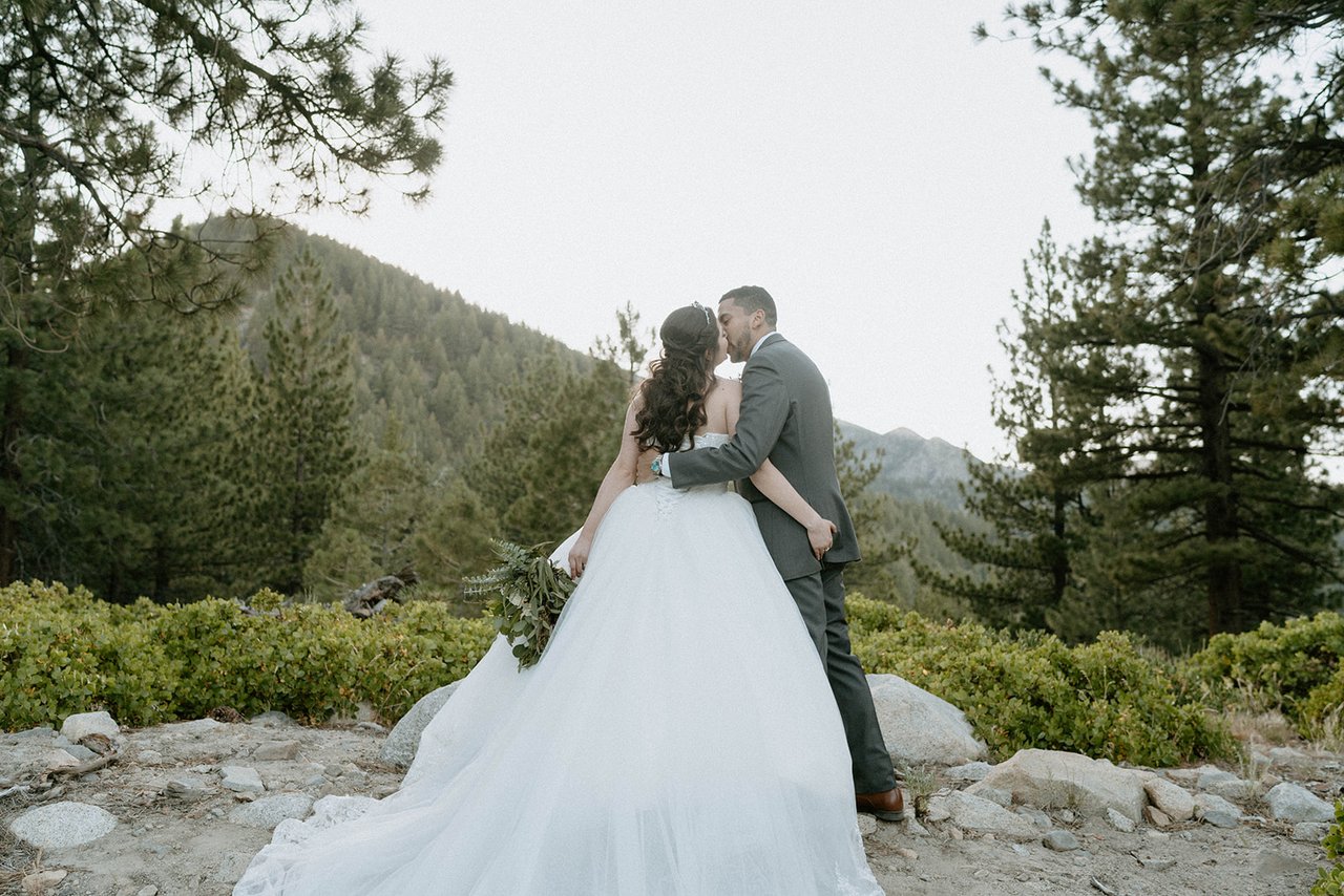 Montse and Jason kiss on the rocks with the mountains and pines behind them