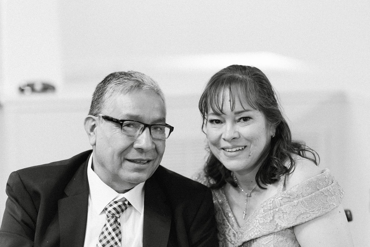 A couple smiles at their table, in black and white