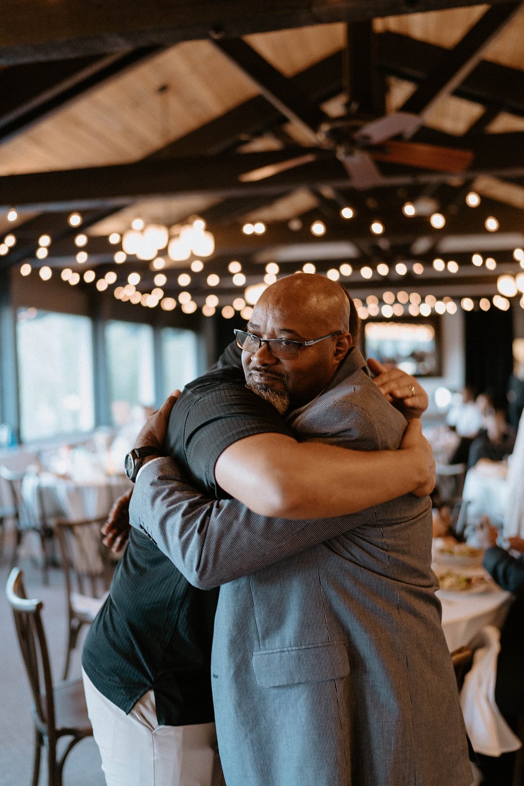 Guests hug under the string lights at the reception