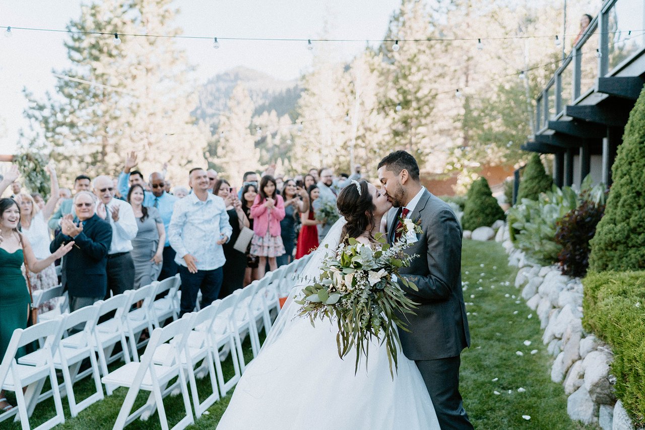 Montse and Jason kiss at the end of the aisle with guests behind them