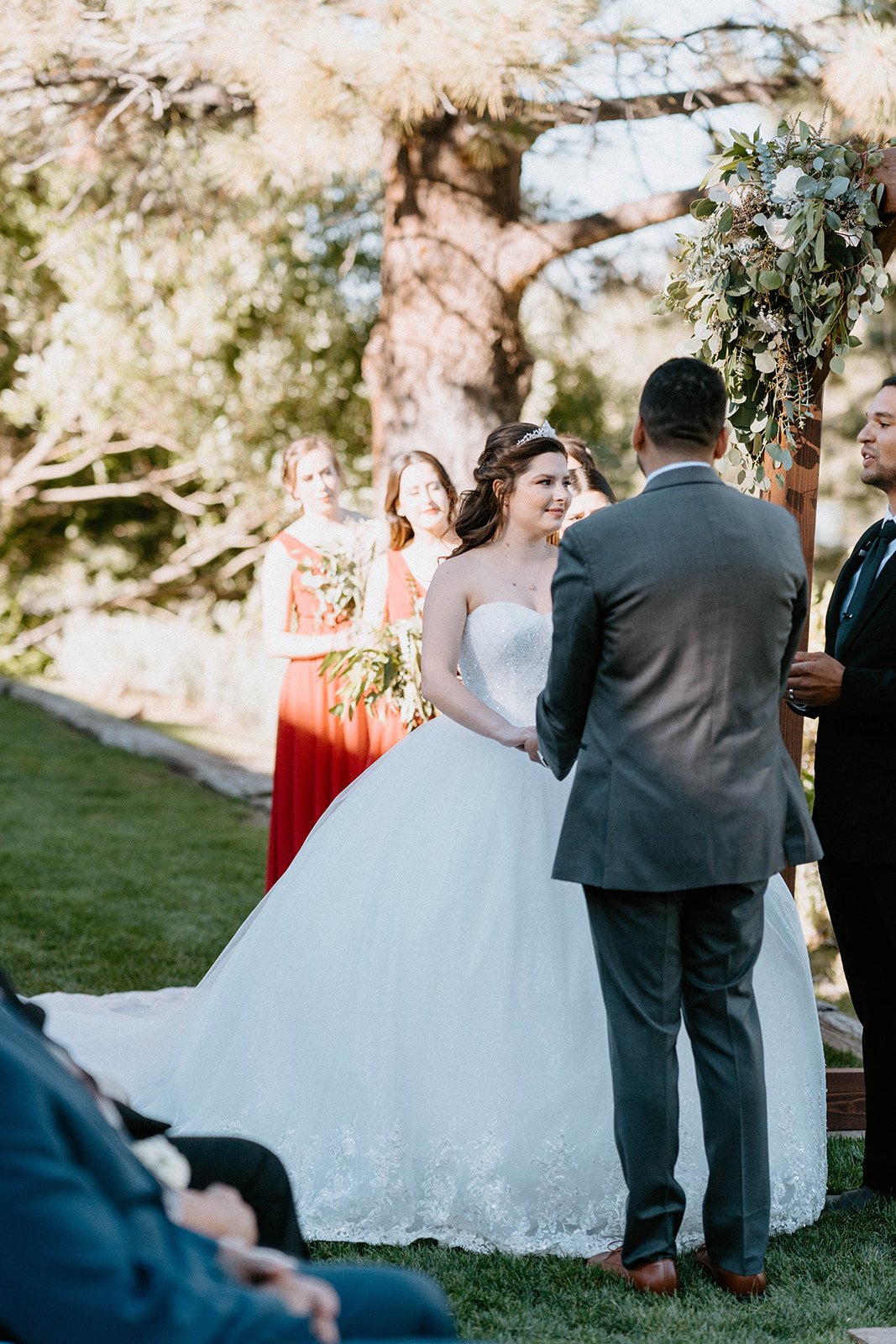 Montse and Jason face each other at the arch under the tall pines