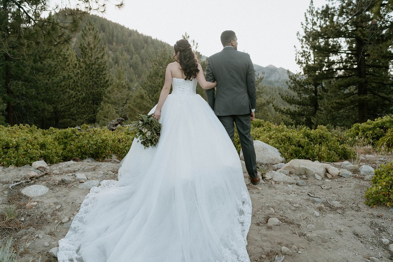 Montse and Jason walk toward the mountains, her gown across the rocks