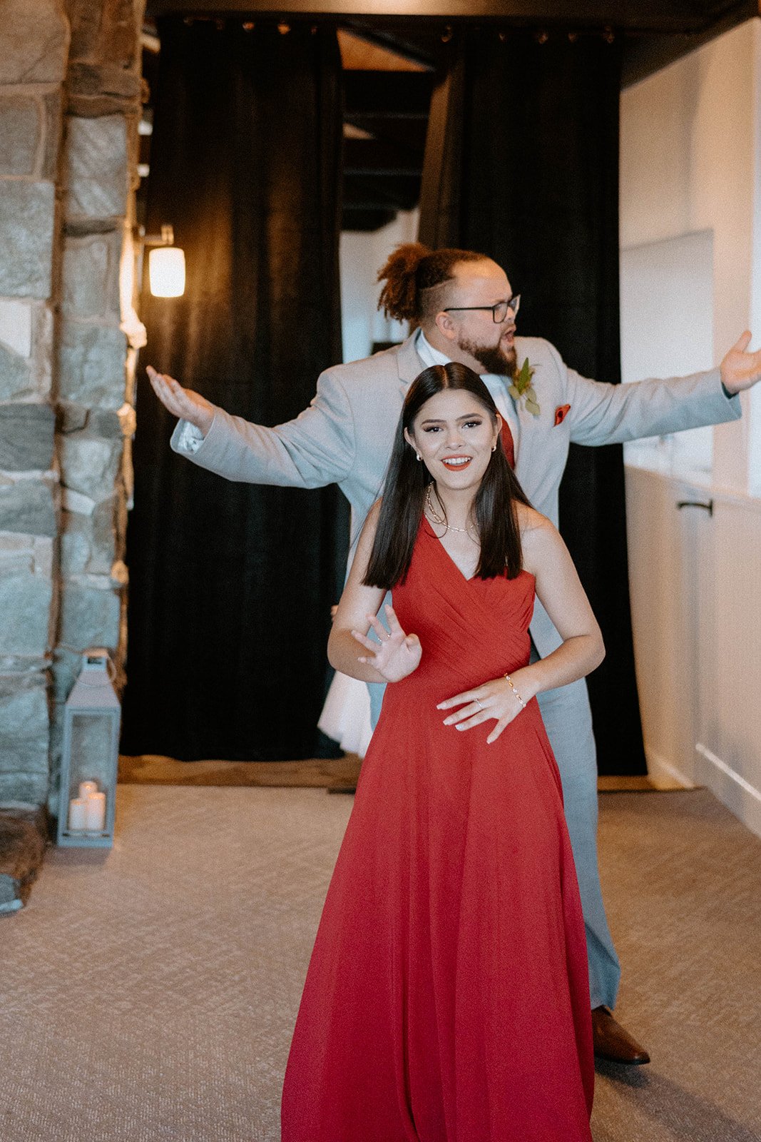 A bridesmaid in red and a groomsman make their entrance with arms wide