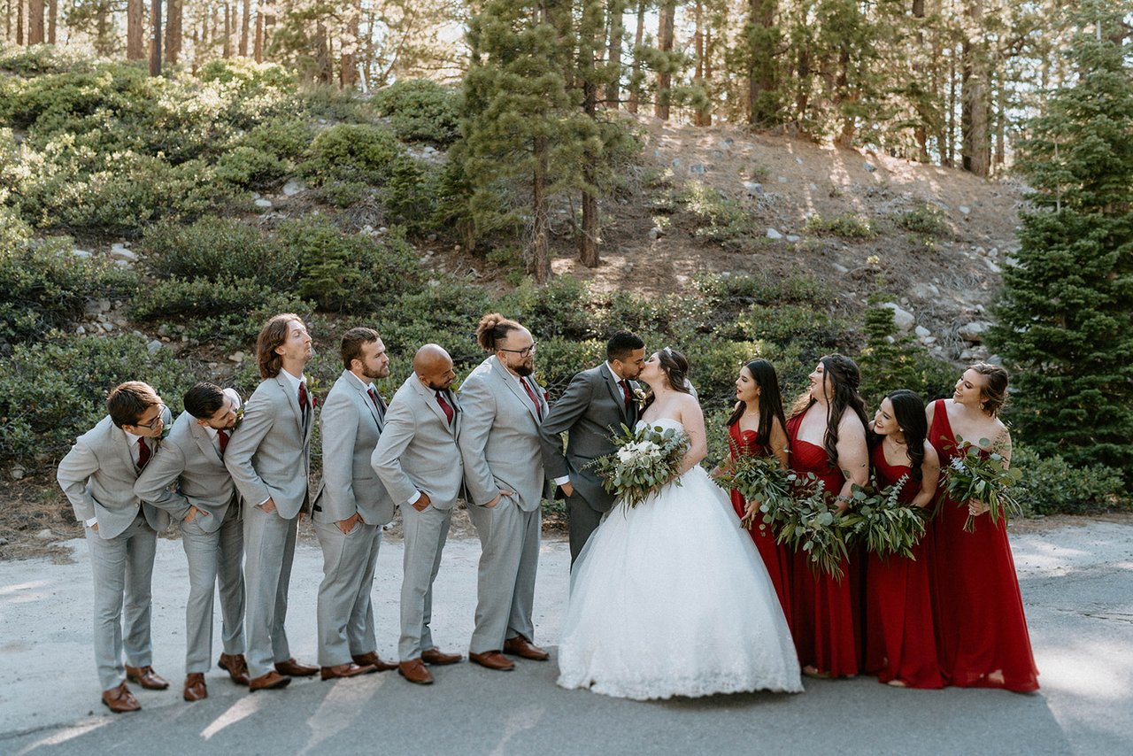 The groomsmen in grey and the bridesmaids in red goof around with Montse and Jason under the pines